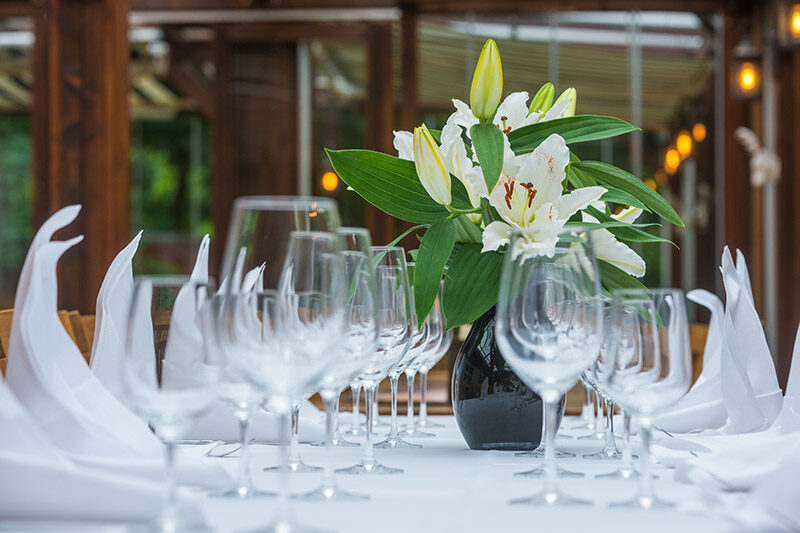 Weiß gedeckter Hochzeitstisch mit vielen Weingläsern und einer Vase mit weißen Lilien als Tischdeko.