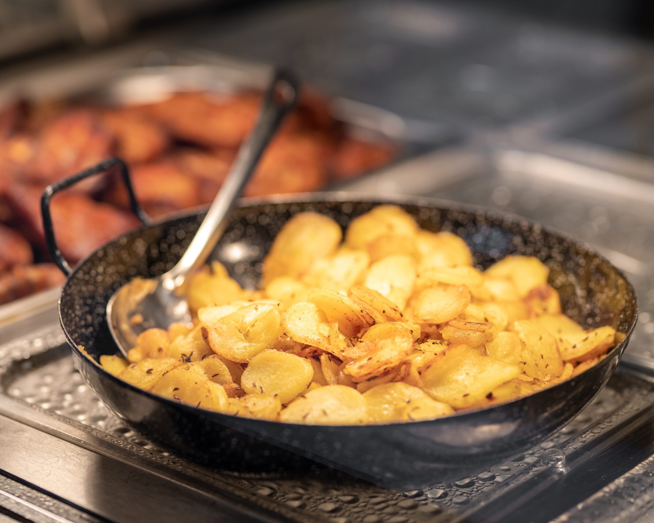 Goldbraune Bratkartoffeln in einer Pfanne am warmen Mittagstisch der Fleischerei Schulze in Dresden, mit Servierlöffel.