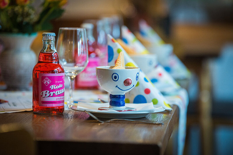 Gedeckter Tisch mit Partyhüten, Flasche Rote Brause und Clown-Eisbecher für eine private Feier.
