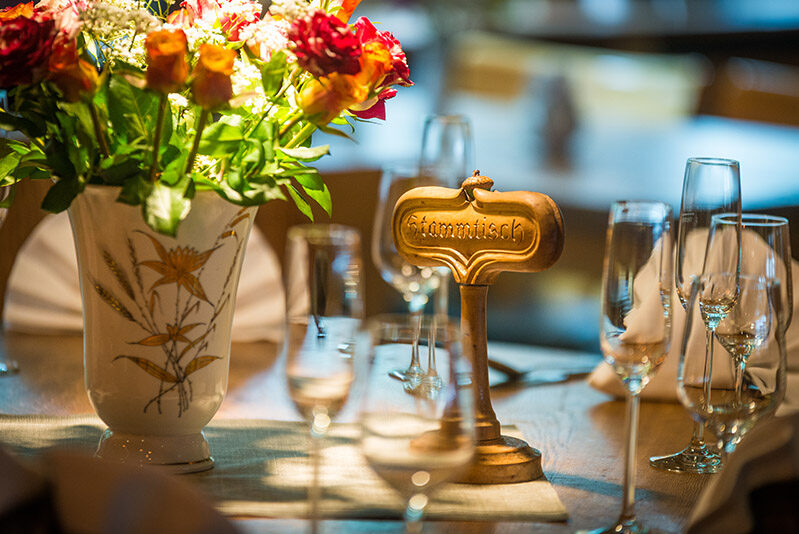 Festlich gedeckter Tisch mit Blumenvase, vielen Gläsern und Tischschild für eine private Feier.