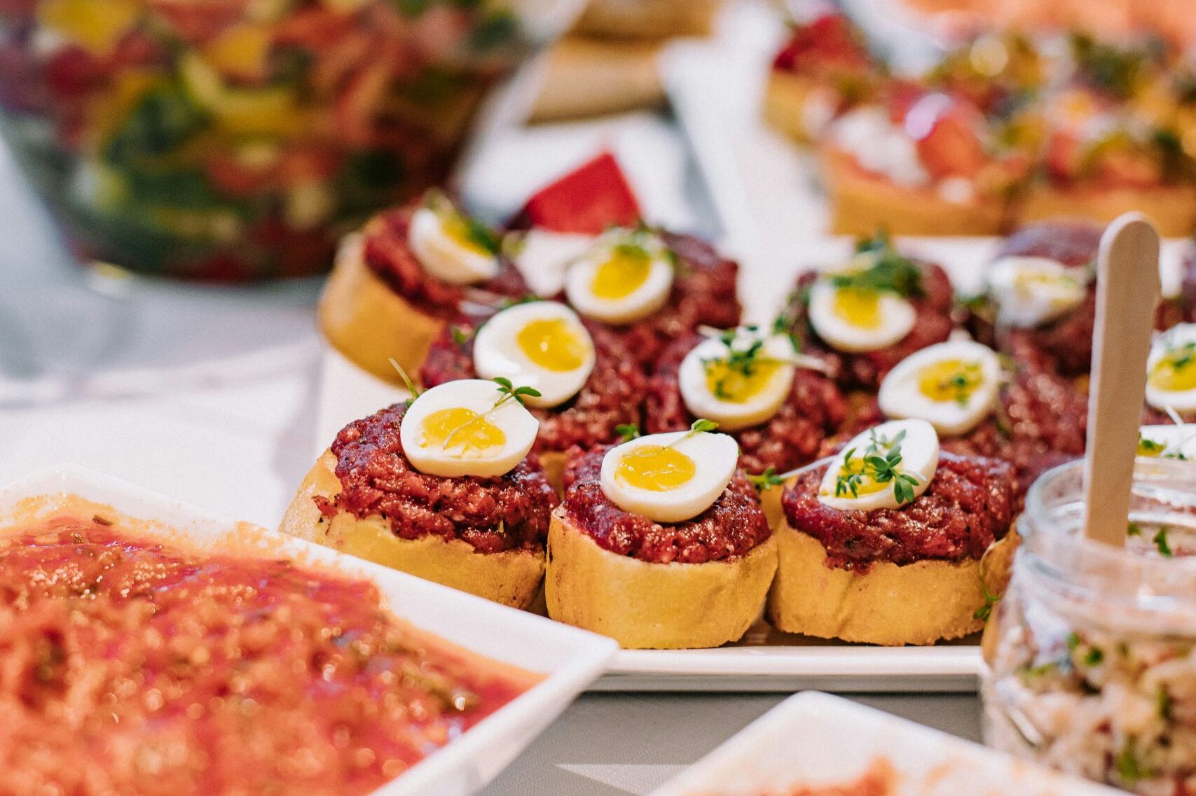 Fingerfood-Buffet mit Canapés, Ei-Scheiben, Kräutern und verschiedenen Dips auf Servierplatten.